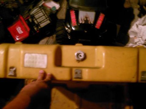 1986 Ford Bronco - A yellow case is in the foreground, with a hand touching it, and a black object with red lettering behind it.