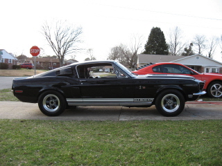 1968 Shelby GT500 - Side view of a black 1968 Shelby GT500 with a red car in the background.
