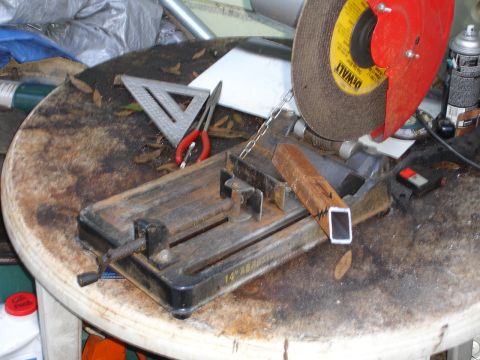 1989 Ford Bronco - Chop saw setup with metal stock. Tools like a square and pliers are nearby on the workbench.