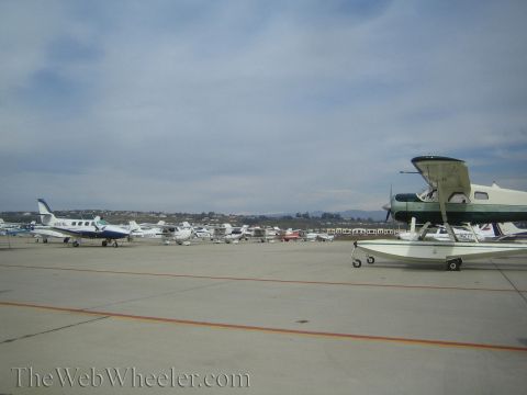 1990 Ford Bronco - Several small private aircraft, including a seaplane on floats, are parked across an airport tarmac under a hazy sky.