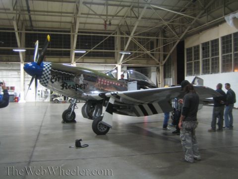 1990 Ford Bronco - bare-metal WWII-style fighter with Grim Reaper nose art and invasion stripes draws onlookers inside a hangar.