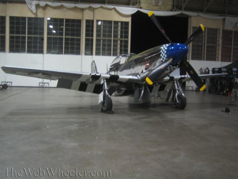 1990 Ford Bronco - polished WWII-style fighter with a blue checkered nose, four-blade prop, and invasion stripes sits inside a hangar.