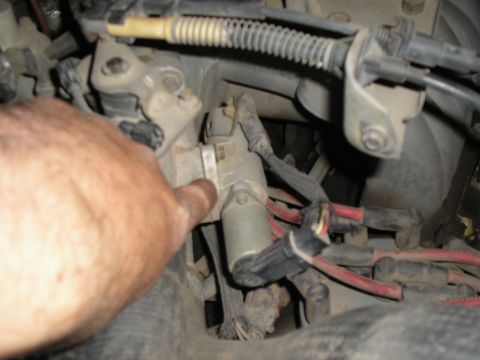 1990 Ford Bronco - A hand points to a component within the engine bay, showing various wires and mechanical parts.