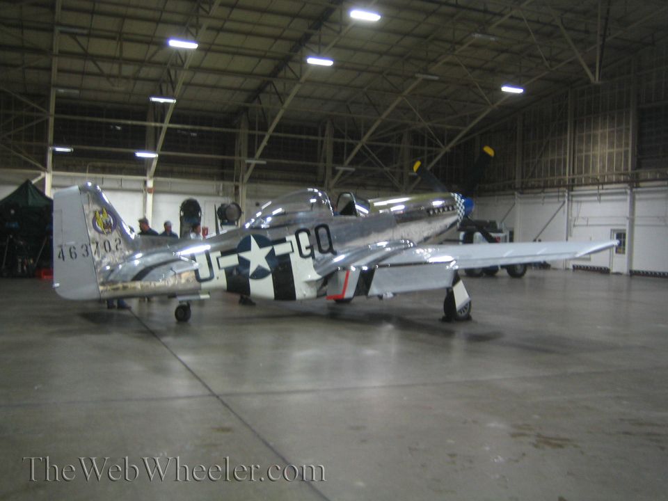Polished WWII fighter plane with US star insignia and serial number in a hangar
