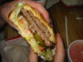 1989 Ford Bronco - A person holds a large double cheeseburger with all the fixings, including lettuce, tomato, and pickles.