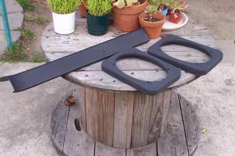 1990 Ford Bronco - Speaker adapter parts and trim piece shown on a wooden spool outdoors.