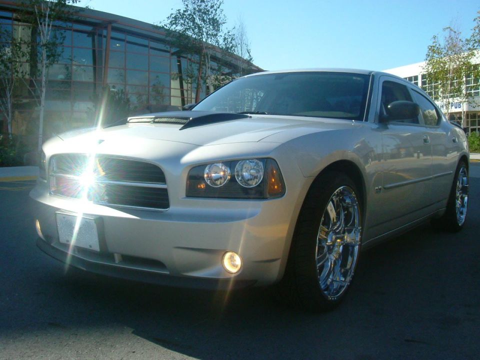 Silver Dodge Charger sedan on chrome wheels, low front three-quarter view in parking lot