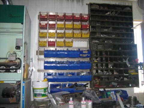 1976 Ford Ranchero - A cluttered garage interior features numerous parts bins and shelves filled with various items.