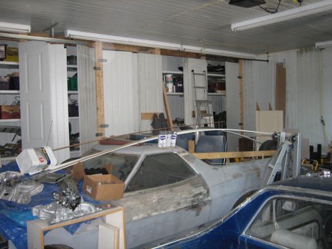 1976 Ford Ranchero - A car in a garage with parts scattered around, showing a primer finish and a partially visible blue car.