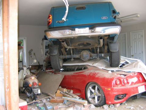 1991 Ford Probe - A blue 1991 Ford F-150 truck is precariously perched atop a red Ferrari, creating a chaotic scene with debris scattered around.