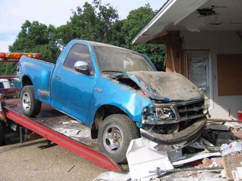 1991 Ford Probe - A damaged blue Ford F-150 pickup truck is loaded onto a tow truck after an apparent collision with a building.