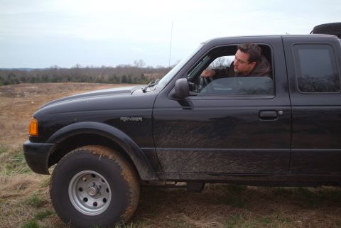 1995 Ford Bronco - Driver's-side profile of a black Ford Ranger extended-cab pickup in a dry grass field, with a person leaning out of the open driver's windo…
