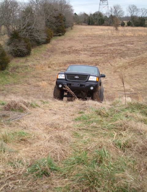 1995 Ford Bronco - A black Ford Ranger navigates a grassy, off-road incline. The grille design indicates an early 2000s model year.