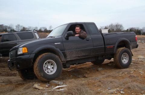 1995 Ford Bronco - A man poses in his black Ford Ranger pickup truck, which is parked off-road with another vehicle in the background.