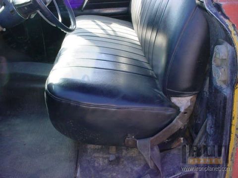 1966 Ford F-250 - The interior of a vehicle shows a worn black vinyl seat and part of the steering wheel.
