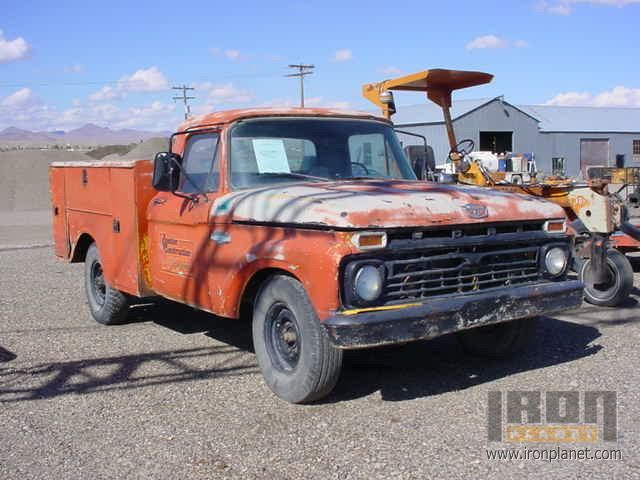 Faded orange 1960s Ford utility service truck with rust on a gravel auction lot