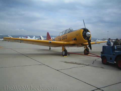 1990 Ford Bronco - yellow single-engine propeller trainer aircraft marked 'TA-920' sits on the tarmac beside a blue tow tractor under overcast skies.
