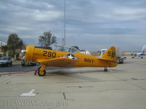 1990 Ford Bronco - yellow propeller trainer marked 'NAVY 290' with a star-and-bar insignia rests on a cracked concrete ramp near other planes.