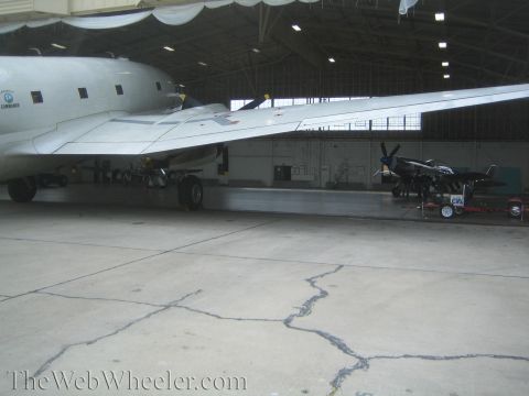 1990 Ford Bronco - large silver multi-engine propeller aircraft and a fighter plane sit inside a spacious hangar with cracked concrete flooring.