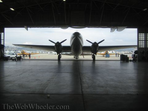 1990 Ford Bronco - twin-engine propeller aircraft is silhouetted head-on in an open hangar doorway, with planes and people visible on the ramp beyond.