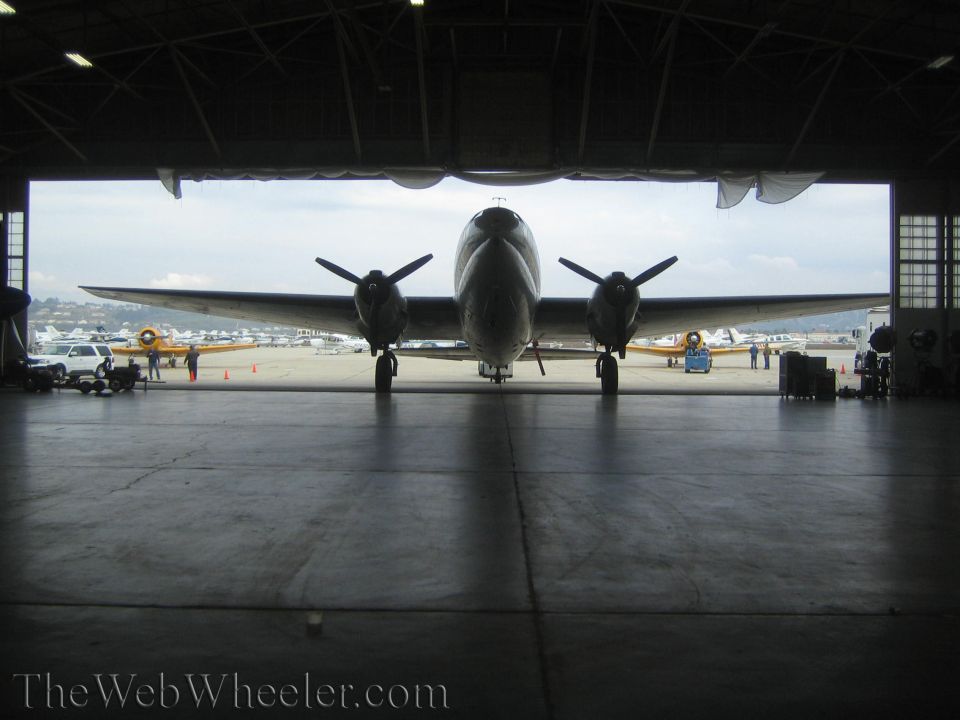 Front silhouette of twin-engine propeller aircraft framed in open hangar doorway