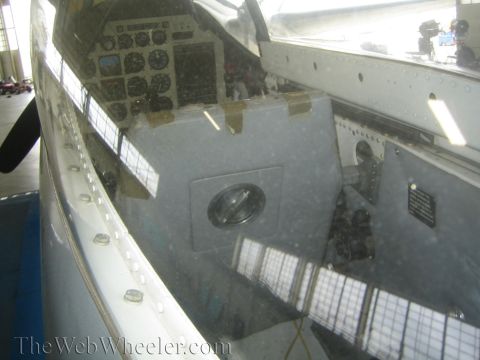 1990 Ford Bronco - reflective close-up through an aircraft canopy reveals the cockpit instrument panel and gauges inside a hangar.