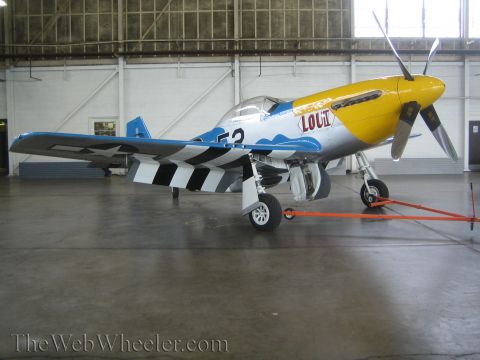 1990 Ford Bronco - silver fighter aircraft with a yellow nose, blue cloud trim, checkered tail and 'LOU II' nose art sits in a hangar.
