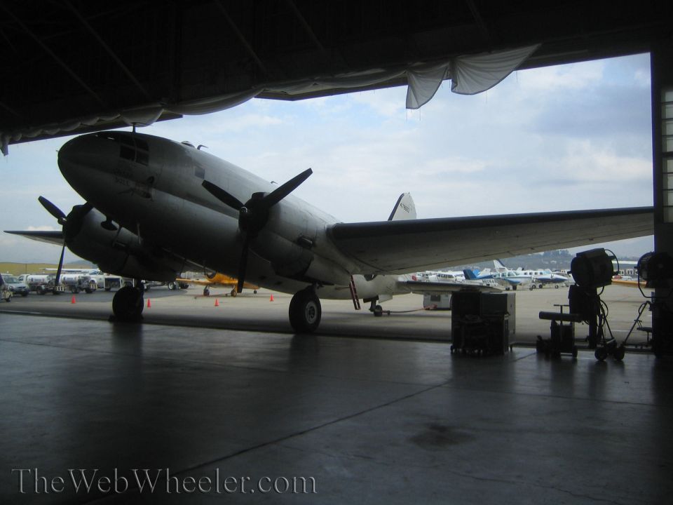 Silver twin-engine propeller transport aircraft parked at open hangar mouth