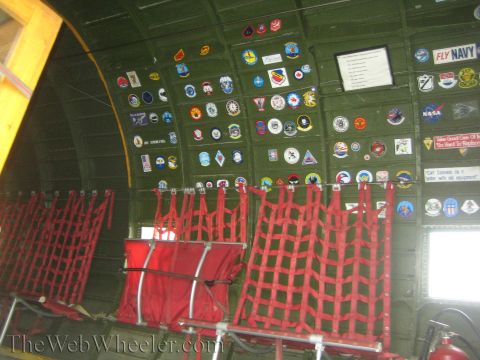 1990 Ford Bronco - green interior cabin of a vintage aircraft shows red webbed troop seats below a wall covered in squadron and unit patches.