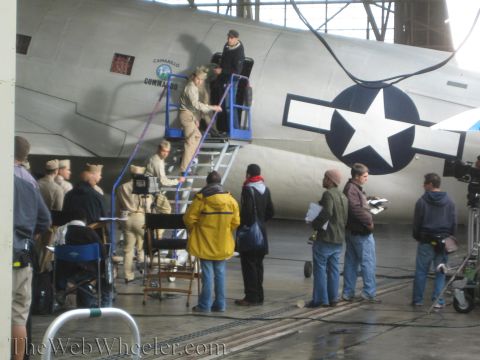 1990 Ford Bronco - film or photo crew in period costume and modern jackets gathers around a large silver aircraft with star insignia inside a hangar.