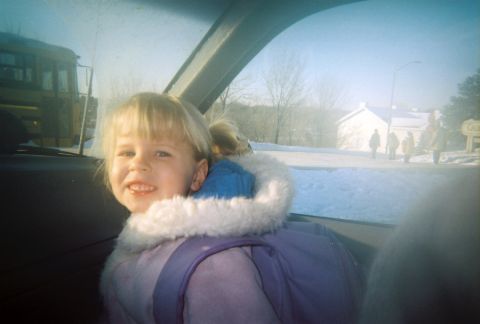 2002 Oldsmobile Aurora - Child in car on a snowy day, with a school bus and houses in the background.