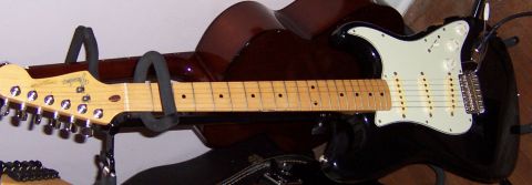 1978 Ford Bronco - A black electric guitar with a maple neck is displayed on a stand, with another guitar body visible behind it.