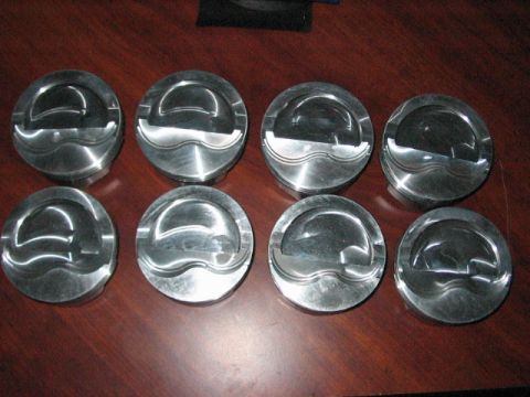 1991 Ford Bronco - A set of eight engine pistons are displayed on a wooden table.