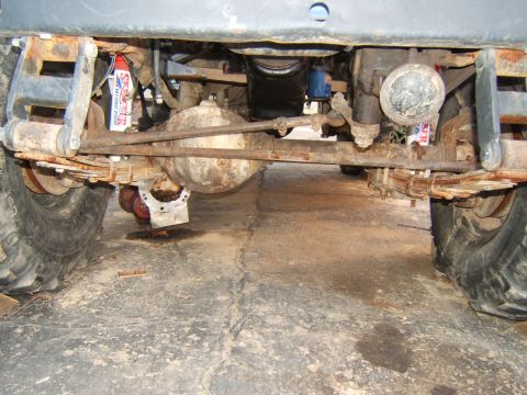 1980 Jeep CJ5 - The underside of a Jeep CJ5 reveals its rear axle, leaf springs, and suspension components, with visible signs of wear and a small fluid le…
