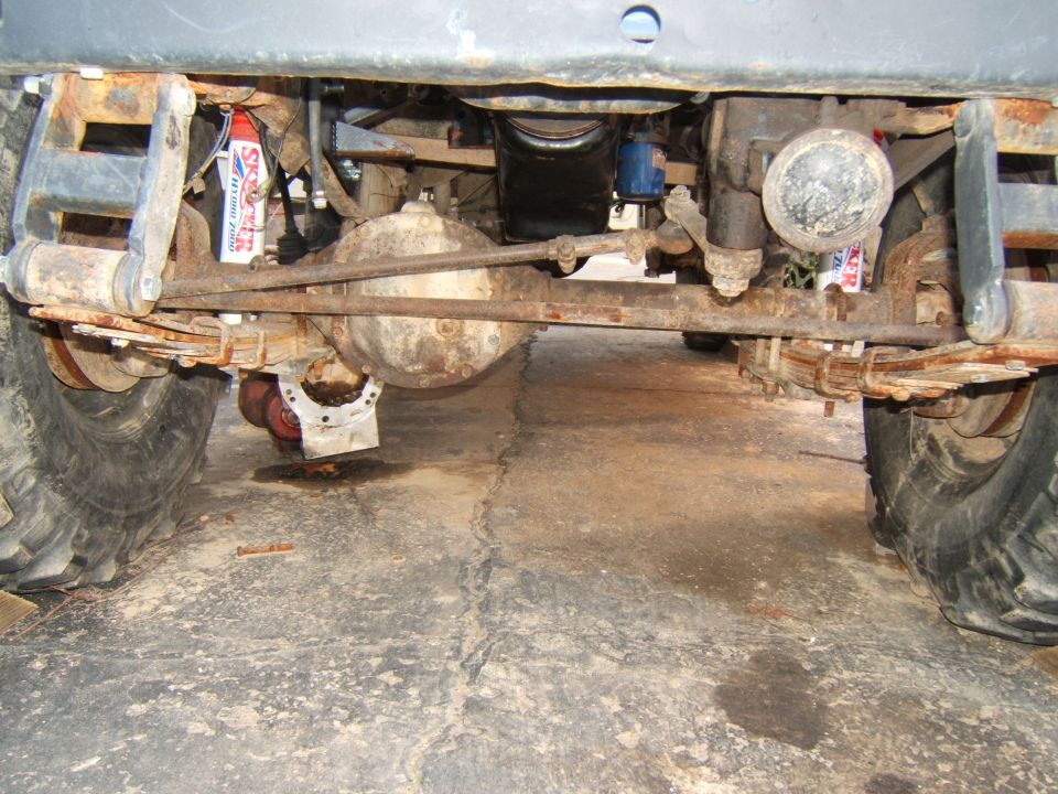 Underneath view of a Jeep CJ5 showing the rear axle, leaf springs, and shocks. Some fluid is leaking