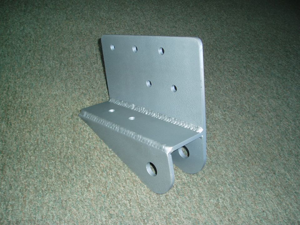 Metal bracket with multiple holes and welded seams, resting on carpet