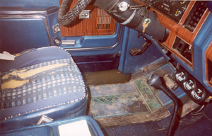 1982 Ford Bronco - The interior of a blue vehicle shows a torn seat, wood-grain trim, and a flooded floor with three gauges visible.