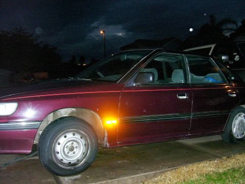 1991 Ford Bronco - A maroon sedan is parked outside at night, showing its side profile with an illuminated amber turn signal.