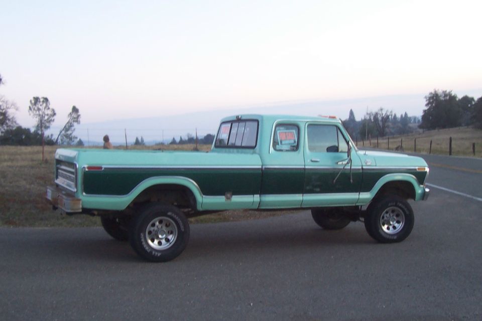 Two-tone green lifted 1970s Ford SuperCab pickup on rural road