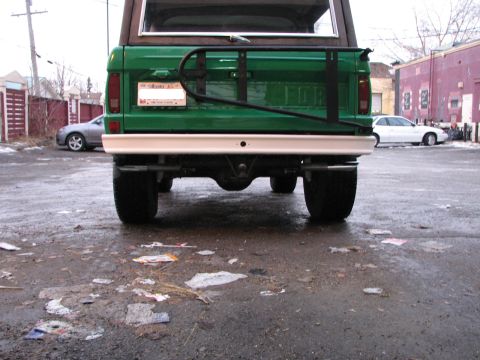 1975 Ford Bronco - The rear of a green SUV is shown, parked on a wet, debris-strewn surface with other vehicles nearby.