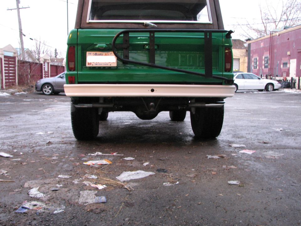 Rear of green SUV with spare tire carrier and white bumper. Two other cars visible in background