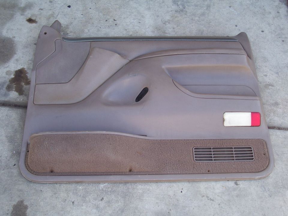Brown plastic car door panel with carpeted lower section and a red/white reflector