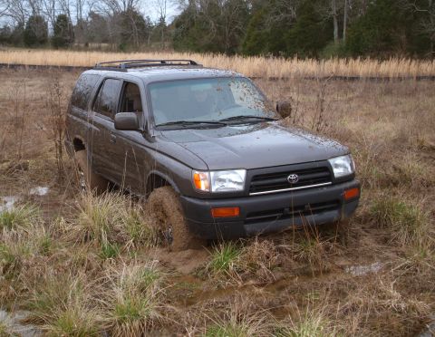 1995 Ford Bronco - Toyota 4Runner stuck in a muddy field with dry grass and trees in the background.