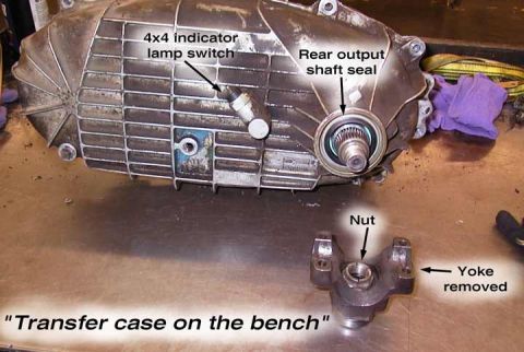 1982 Ford Bronco - Transfer case on the bench, showing the 4x4 indicator lamp switch and rear output shaft seal, with a separate yoke removed part.