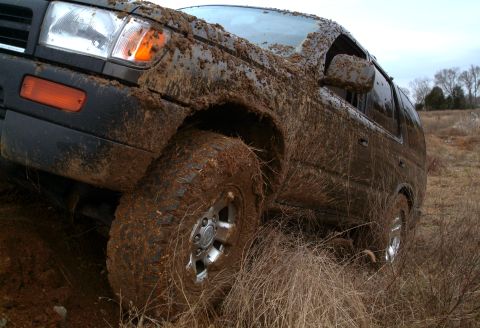 1995 Ford Bronco - SUV covered in mud, stuck in tall grass off-road.