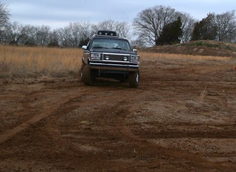 1995 Ford Bronco - A black Ford Bronco navigates a muddy off-road course under an overcast sky.