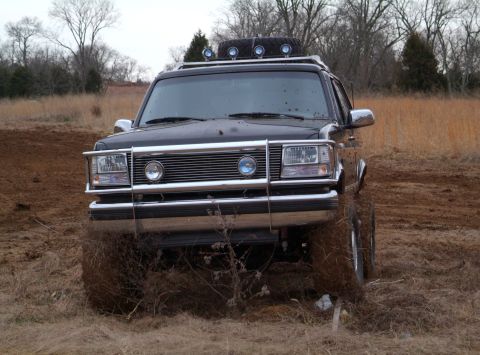 1995 Ford Bronco - Head-on front view of a lifted black Ford Bronco sitting in a muddy field, hood and windshield freshly spattered with mud clods after wheel…