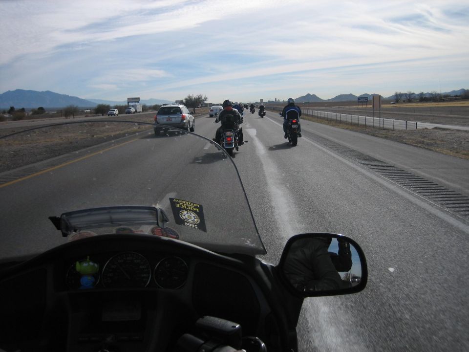 View from a motorcycle windshield looking at a convoy of motorcycles and cars on a highway under a partly cloudy sky