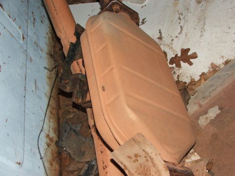 1965 Ford Mustang - This image shows a close-up view of a rusty exhaust system component, likely a muffler, mounted with metal brackets.