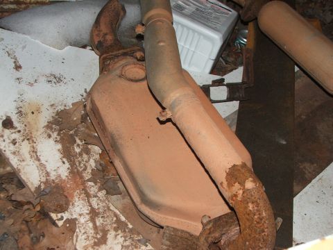 1965 Ford Mustang - A rusty exhaust system part, possibly a catalytic converter, lies on a debris-covered surface.